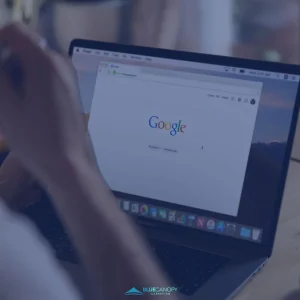 Person mostly out of frame viewing the Google search home page on a black laptop computer.